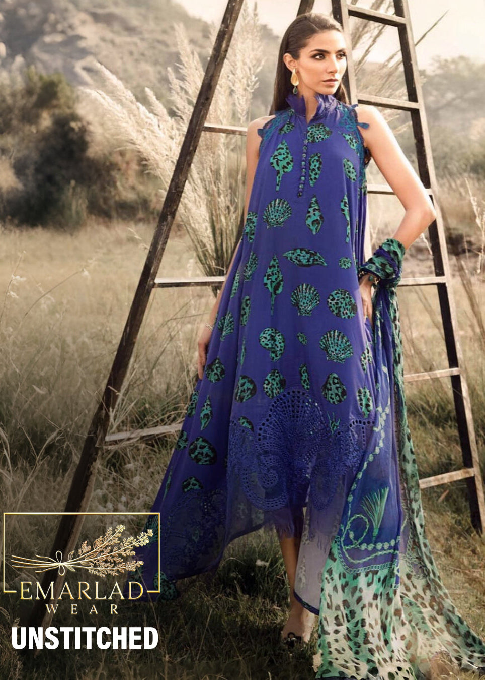 Woman in a blue and green dress standing next to a ladder in a natural setting with 'Emarlad Wear' branding.