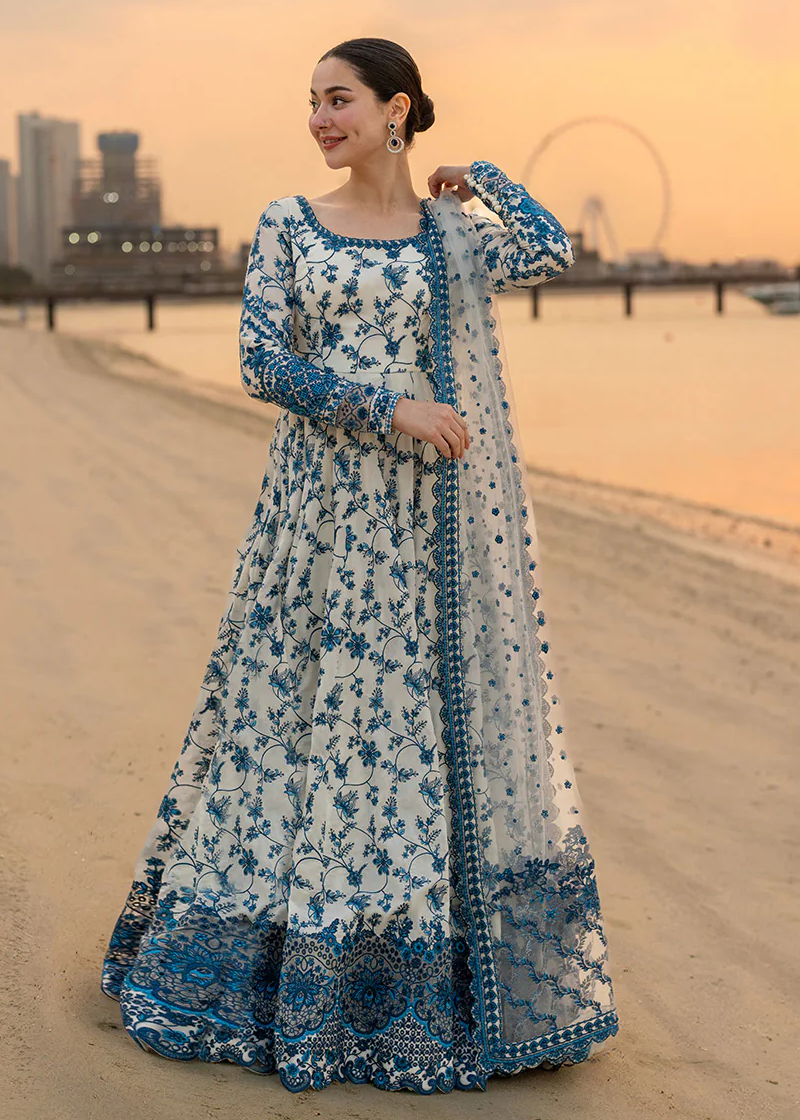 Woman in a blue and white floral dress standing on a beach with a cityscape in the background.