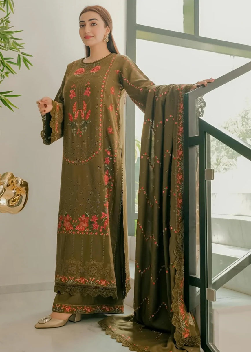 Woman wearing an embroidered green outfit standing indoors with a glass door in the background.