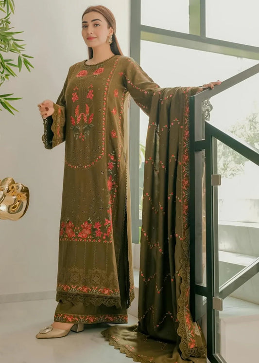 Woman wearing an embroidered green outfit standing indoors with a glass door in the background.