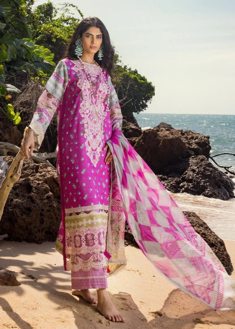 Woman in a pink and white embroidered outfit standing on a rocky beach.