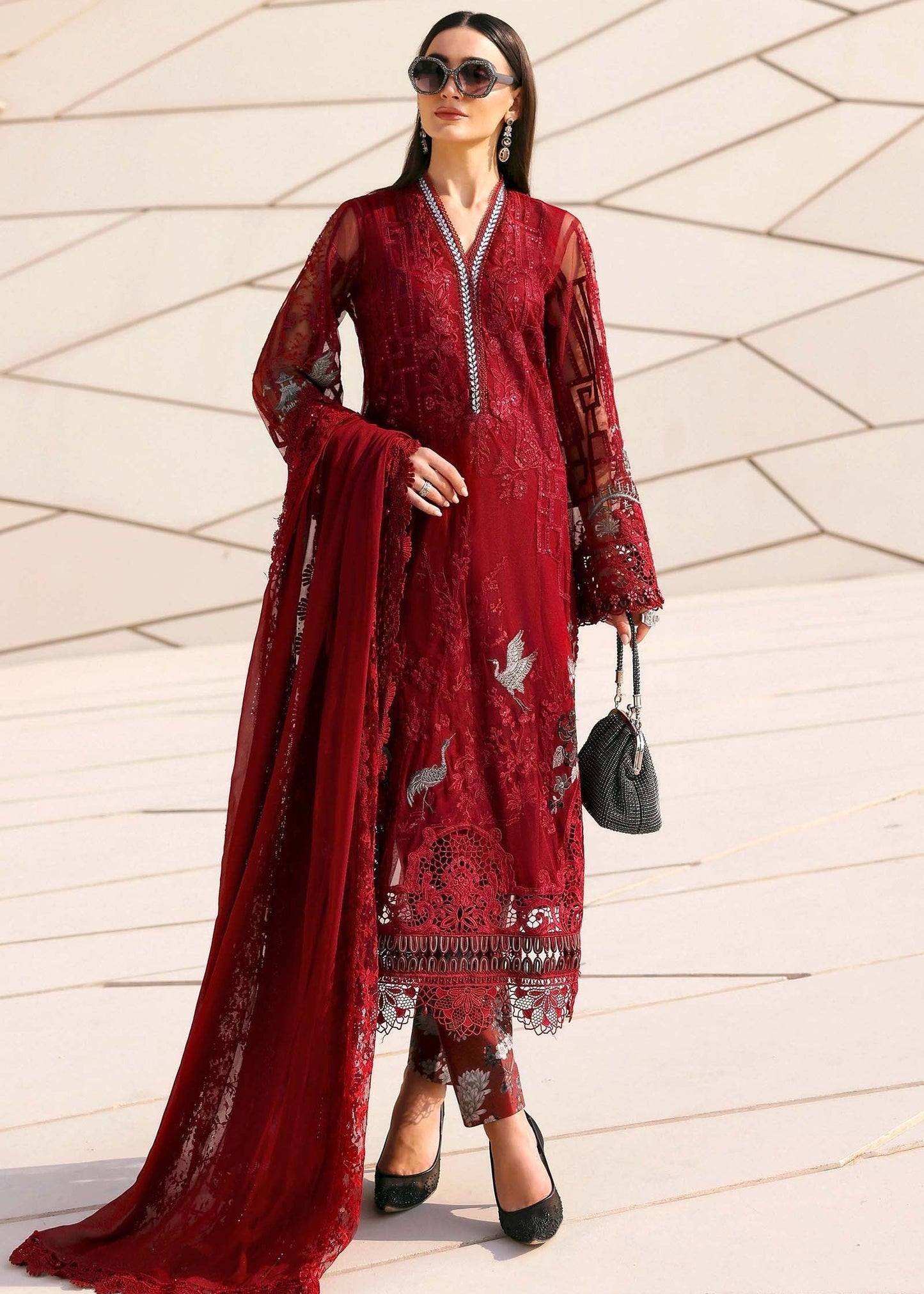 Woman wearing a red embroidered outfit with a matching dupatta against a geometric-patterned wall.