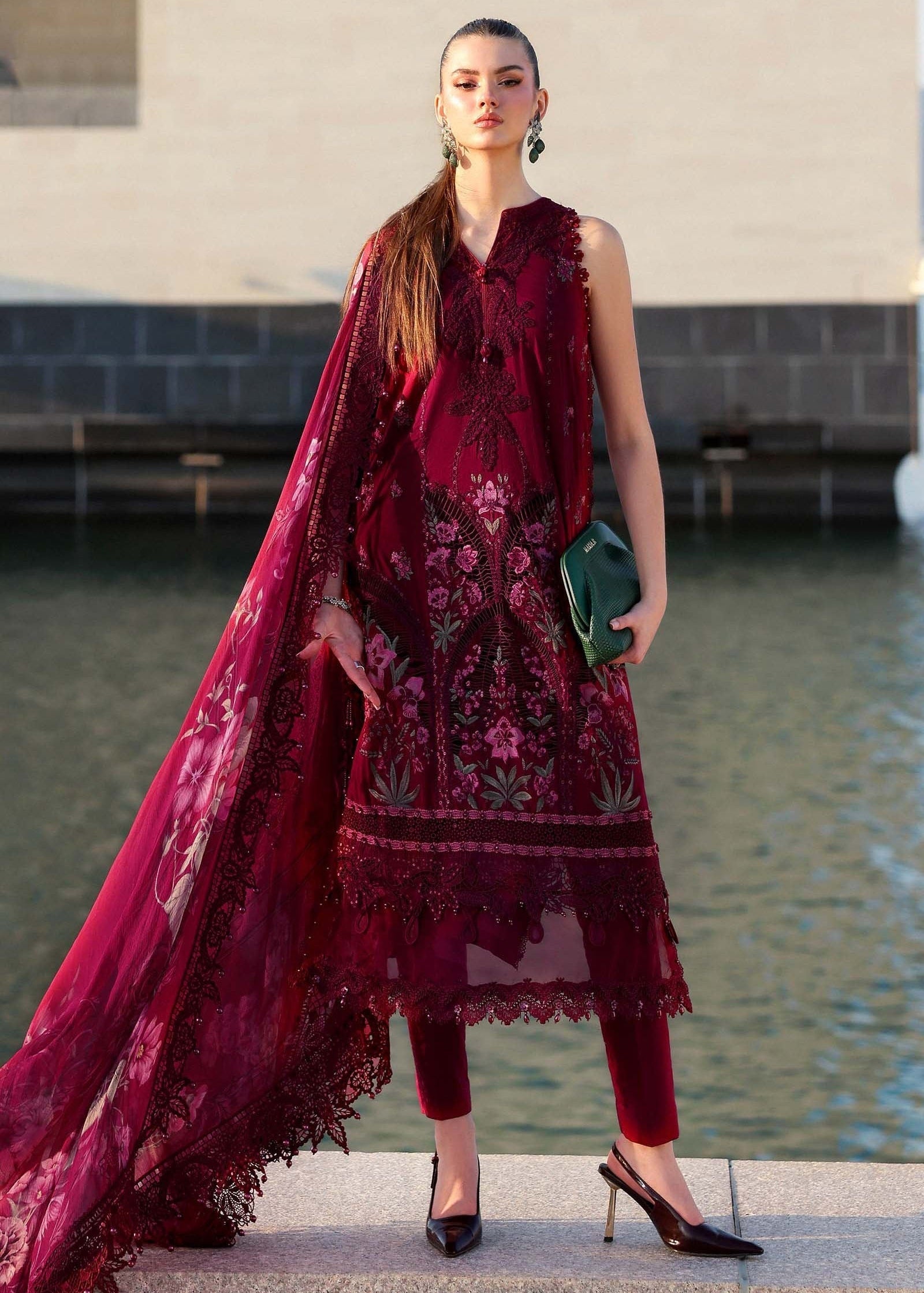 Woman in a burgundy embroidered outfit standing by a body of water.