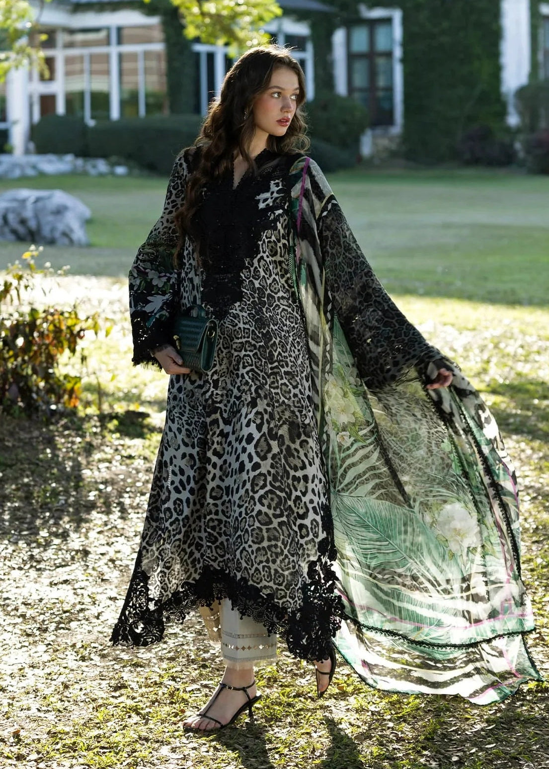 Woman in a long, patterned coat standing outdoors with a house and garden in the background
