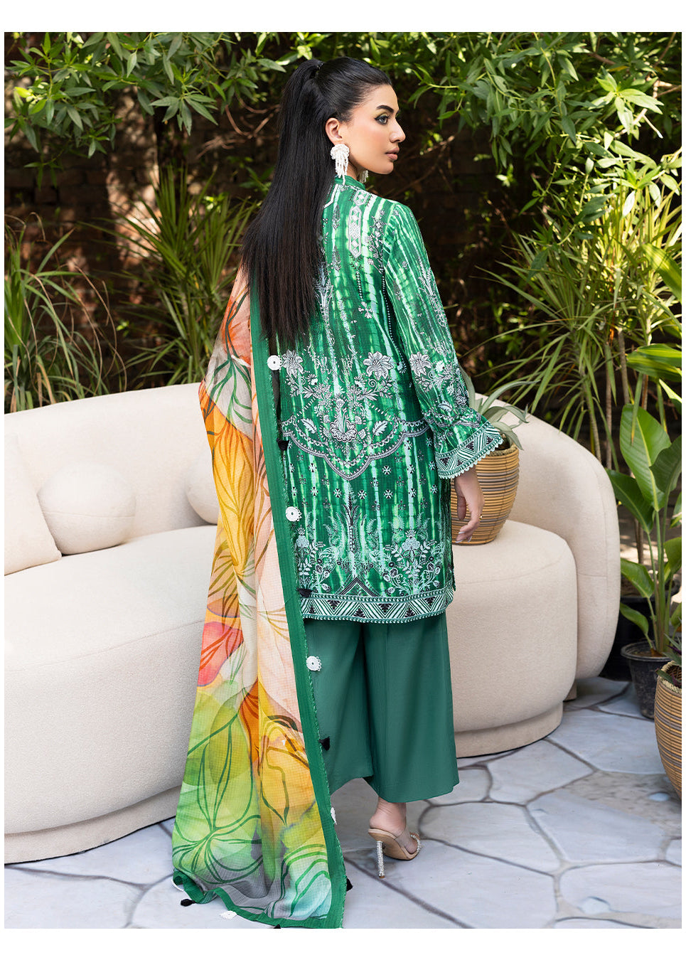 Woman in a green outfit with floral patterns standing outdoors near a white couch.