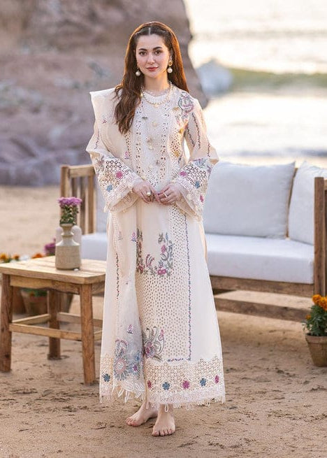 Woman in a white embroidered dress standing on a sandy beach with a wooden table and sofa in the background.